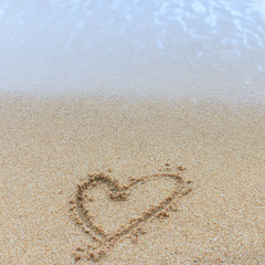 A heart symbol written on a sandy beach with foam and water background. Valentines day concept. 