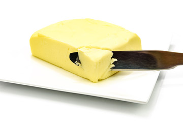 Piece of butter with silver knife on the plate isolated on a white background in close-up 