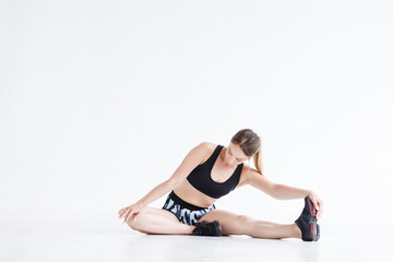 Fototapeta na wymiar Beautiful young athletic girl doing exercises for stretching the ligaments and muscles of the legs before training sitting on the floor in the gym