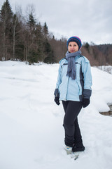 Fototapeta na wymiar girl in pants, jacket, gloves and scarf standing in the snow in front of the forest