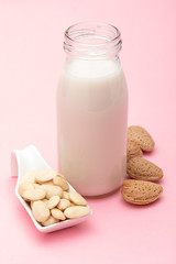 Almond milk in glass bottle. Includes peeled and peeled almonds. On light pink background.