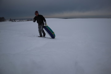 young man on a snowy hill with inflatable snow tube