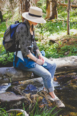 girl in sunhat sitting on log above stream