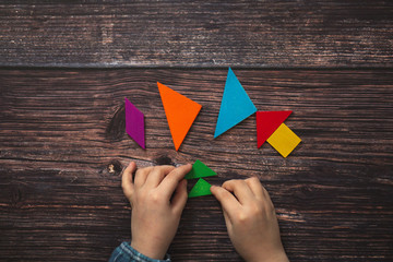 children's hands and wooden tangram game on wooden
