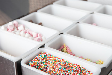 Different colorful sweet toppings in white trays in the restaurant
