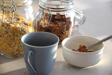 Blue cup, bowl with yoghurt and cornflakes and jars of cereals and muesli