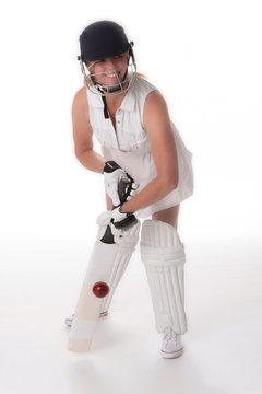 Woman cricketer in a white dress with a safety helmet, shin pads, a bat and ball.