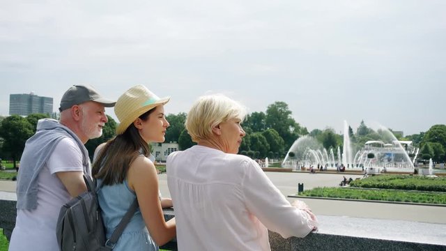 Back view of happy family enjoying summer vacation together in Moscow, Russia. Seniors with young teenage daughter having great time standing in Gorky Park laughing and chatting sightseeing