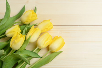 Bouquet of yellow tulips on a raw wood background, flat lay view from above, with space for text, for Valentine's Day or Mother's Day