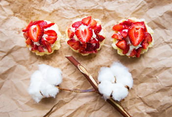 Fototapeta na wymiar Beautiful cupcakes with strawberries along with a branch of cotton lies on kraft paper
