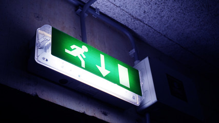 Glowing on a green background sign Exit with a down arrow, a running man in a brick building by the door in dark colors