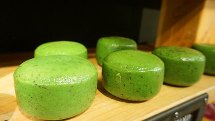 6 heads of green spicy cheese with herbs and pesto stand on a wooden shelf in the cellar on maturation or sale