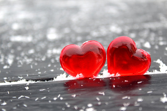 Two red plastic hearts on a black background studded with white snowflakes