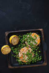 Above view of fried fish medallions with green peas and lemon, vertical shot on a black stone background, copyspace