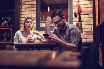 Young smiling couple in gorgeous restaurant. Man looking at phone. - Image