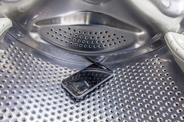 a cell phone with a broken display that falls out of a pocket of clothes lies inside the drum of a...