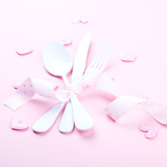 Festive table setting for Valentines Day with fork, knife and hearts  on pink pastel background.Romantic dinner. Space for text.