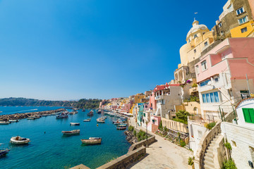 Fototapeta premium Szeroki kąt zdjęcia tętniącego życiem kolorowe mieszkania, wędkarstwo i zwiedzanie łodzi, kawiarni i restauracji w Marina Corricella w słoneczną pogodę latem na wyspie Procida, Włochy.