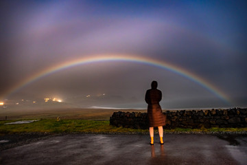 Lady observing very rare moonbow during the night above Staffin bay - Isle of Skye, Scotland