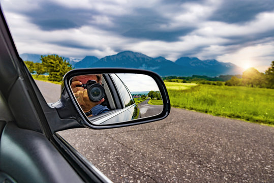 Reflection of a photographer with a camera in the rear view mirror of a car in nature.