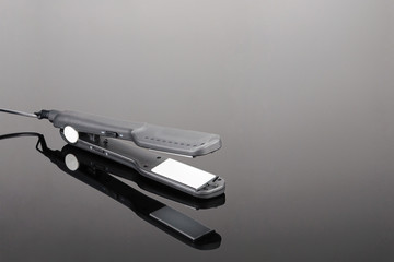 Grey hair iron on the grey mirror background