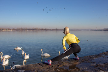 young woman jogging and workout by the river full of swans in city 