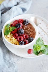 Sunday Breakfast. Oatmeal porridge with banana and flax seed, raspberries, blackberries, corn flakes, honey and mint, selective focus. Useful food, diet. Plate or cup with vegan porridge, smoothies 