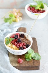 Sunday Breakfast. Oatmeal porridge with banana and flax seed, raspberries, blackberries, corn flakes, honey and mint, selective focus. Useful food, diet. Plate or cup with vegan porridge, smoothies 