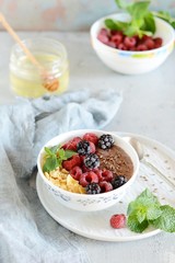 Sunday Breakfast. Oatmeal porridge with banana and flax seed, raspberries, blackberries, corn flakes, honey and mint, selective focus. Useful food, diet. Plate or cup with vegan porridge, smoothies 