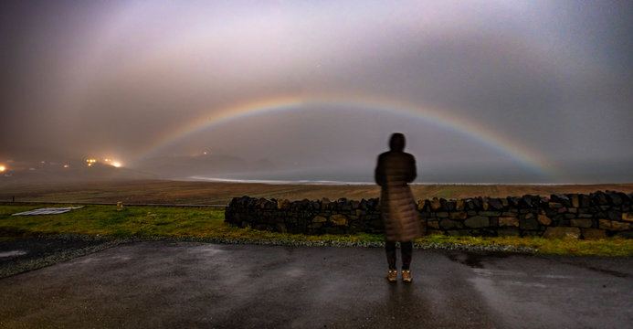 Lady observing very rare moonbow during the night above Staffin bay - Isle of Skye, Scotland