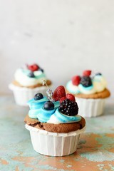 Chocolate cupcaks with vanilla cheese cream and berries on an old background, selective focus