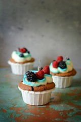Chocolate cupcaks with vanilla cheese cream and berries on an old background, selective focus