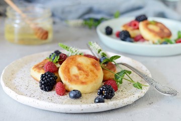  Sunday breakfast with cheesecake, honey, fresh berries  and mint. Cottage cheese pancakes or curd fritters decorated honey and berries in plate on blue table top view. Healthy and diet breakfast.