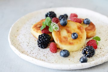  Sunday breakfast with cheesecake, honey, fresh berries  and mint. Cottage cheese pancakes or curd fritters decorated honey and berries in plate on blue table top view. Healthy and diet breakfast.