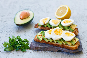 The concept of proper nutrition. Toasts with avocado, lemon, chilli or paprika and eggs on a gray background