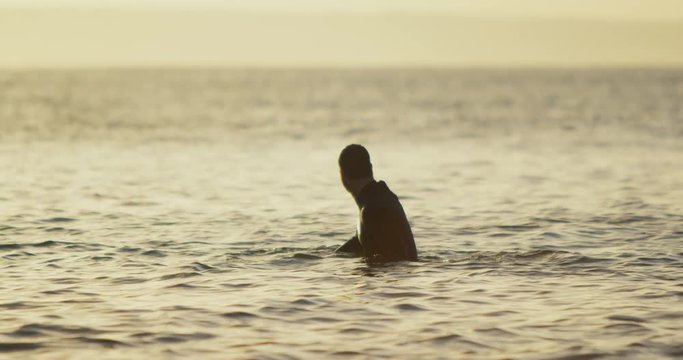 Side view of mid-adult caucasian male surfer sitting over surfboard in sea during sunset 4k