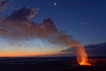 Obraz premium A view of an active volcano at dawn, with orange glow from the lava and the early morning sky in the background. It is the Kilauea volcano on Hawaii’s Big Island, before the 2018 eruption.