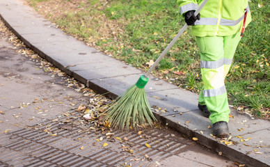 municipal worker sweep the road with broomstick and collects garbage in scoop. sanitation worker sweep street