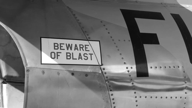 Tilt down to BEWARE of BLAST near engine of 1950s fighter jet. F-86 Sabre. Black and white.Handheld shot with stabilized camera.