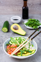 Salmon poke with avocado,  arugula and cucumber in a bowl and chopsticks