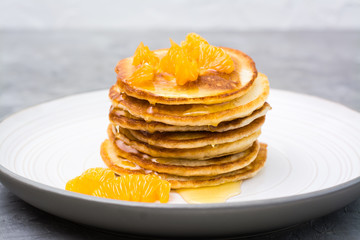 Delicious homemade pancakes with tangerines and honey on a plate on the table. Close-up