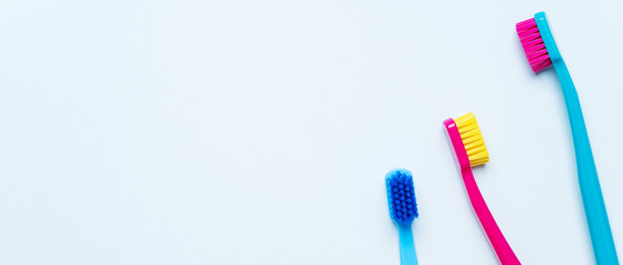 Colorful tooth brushes with bright color bristles on a light pastel blue background. Long wide banner for your mock up with dental tools and empty space for text.