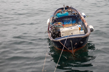 Fototapeta na wymiar Fishing boat with deep blue accent surrounded by buoy and net inside. Anchored on water next to shore with ropes.