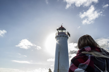 A young woman dressed in black is looking towards a white lighthouse , Great Ocean Road