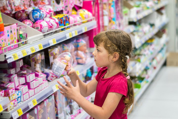  Little girl buys a plastic toy egg in a supermarket. Baby takes a gift from the store shelf. A...