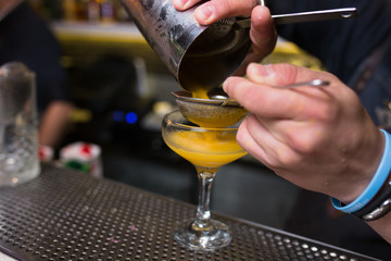 Orange Cocktail being poured at a bar preparing a drink. Motion blur of the bartender's hand and strainer. Selective focus on the foreground glass. Trandy barman  black stylish style