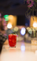 Red Cocktail drink-beverage on  a bar.  Selective focus on the foreground glass,night background . Blurred people in the background.  Trendy black stylish  edit. Copy paste space for design concept