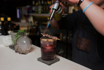 Fototapeta na wymiar Exotic healthy Cocktail, bartender with blaze blowtorch burning decoration meat, mint beverage on a bar counter. Selective focus. Trendy stylish edit. Copy paste space design service barman