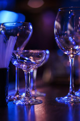 Glasses on the bar counter during a party. Transparent clean glasses in neon light on the bar prepared for drinks. 