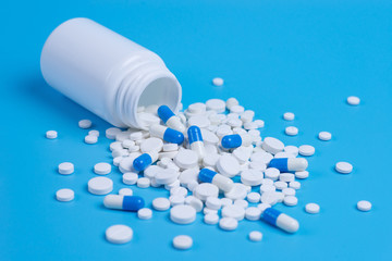 White and blue pills, tablets and white bottle on blue background.